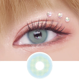 A close-up of a blue-green eye with a heart-shaped highlight, long lashes, pink glitter eyeshadow, and three rhinestones above the brow. Below is the EyeCandys Pink Label Mykonos Blue contact lens with a similar pattern.