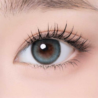 A close-up of a human eye with long lashes wearing i-Girl One Pick Becca Matcha Blue contacts, revealing detailed iris patterns and smooth, light skin around the eye for a subtle, natural finish.