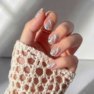 A hand with glittery, floral Birthday Cake Press-On Nails by EyeCandys is partly covered by a cream crocheted sleeve—these playful, sheer gel nails add a funfetti touch to your look.