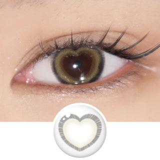 A close-up of an eye wearing EyeCandys Brown Heart contact lenses by EyeCandys, featuring a heart-shaped brown design in the iris with the pupil centered; a separate view of the lens is shown below the eye.