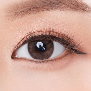 A close-up of an eye with long lashes and natural makeup showcases the Olola Mellows 1-Day Muse Brown (10pk) contact lens by Olola, blending seamlessly while hydrating lenses provide comfort and clear vision.
