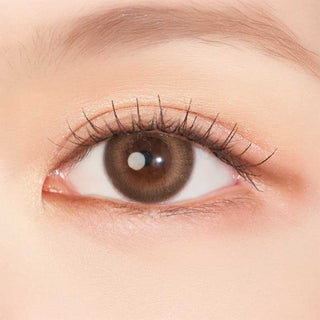 A close-up of a brown eye with long lashes, smooth skin, and natural makeup, enhanced by Clalen IRIS Canola Brown (10pk) colored contacts from Clalen.