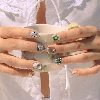 Hand wearing EyeCandys Cottage Core press on nails featuring earthy tones, floral nail art, and green cat eye and chrome accents.