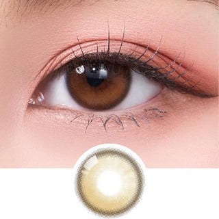 A close-up of a brown eye wearing Olola Dahlia Brown by Olola, featuring the natural-looking brown non-prescription contact lens design below. The makeup is soft with peach-toned eyeshadow and defined eyelashes.