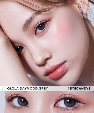A close-up of a woman shows Olola Daymood Grey color contact lenses for dark eyes, pink blush, soft pink lips, and subtle eye makeup. She rests her head on her arm. Text: "Olola Daymood Grey" and "#EYECANDYS." Myopia prescription available.