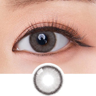 A close-up of an eye wearing Olola Dearsome Ash Grey contact lenses by Olola, ideal for dark eyes with long lashes and subtle makeup. Below the eye is an enlarged view of the same grey lens.