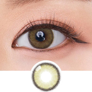 A close-up of a brown eye wearing Olola Dearsome Olive Green contacts by Olola, perfect for dark eyes. Long lashes and subtle makeup enhance the look, with a circular image below showing the unique lens design.