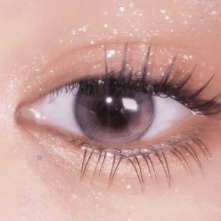 A close-up of an eye wearing EyeCandys Limited Edition Amelie Sakura Jelly Pink contacts, with long lashes and shimmery, glittery eye makeup enhancing the eyelid and surrounding skin.