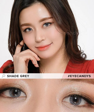 A woman with long dark hair and light makeup smiles gently, wearing EyeCandys Shade Grey colored contacts. A close-up below highlights her eyes with the lenses, shimmering eyeshadow, and defined brows. Text: "EyeCandys Shade Grey.