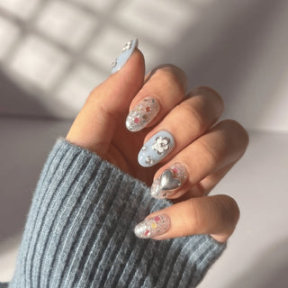 Hand wearing EyeCandys Fleur de Slay press on nails featuring powder blue nails, chrome heart accent, and glitter confetti details.