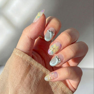 Hand wearing reusable Floreline press on nails featuring pastel flower nail art, sheer base, mint shimmer accent, and delicate pearl details.