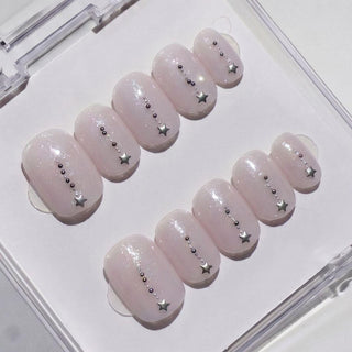EyeCandys Gemini Press-On Nails feature pale pink shimmer press-ons, each adorned with a vertical row of metallic beads and a silver star at the tip. The reusable nails come neatly arranged in a clear box.