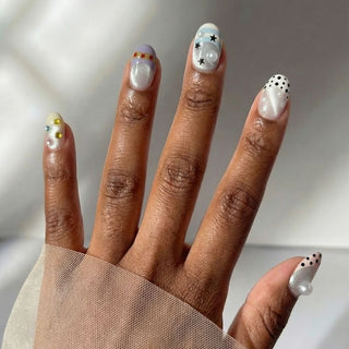 Hand wearing EyeCandys Headliner press on nails featuring silver shimmer base, rhinestones, star designs, and bold festival nail art.