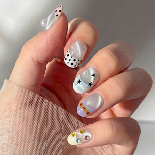 Close up hand showcasing Headliner press on nails with silver chrome shimmer, polka dot pearl nail, and multicolor rhinestone accents.