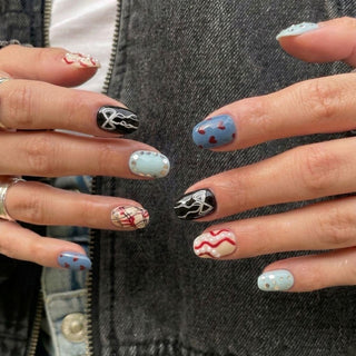 Close-up of hands wearing EyeCandys Heartbreak Hotel Press-On Nails in blue with pearls, black with abstract lines, red hearts on blue, plaid, and red squiggles on cream. Rings and denim complete this salon gel manicure look.