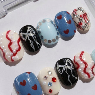 The Heartbreak Hotel Press-On Nails by EyeCandys feature handmade designs with red hearts, pearls, rhinestones, silver dots, bows, wavy lines, plaid accents, and bold black, blue, and white backgrounds.