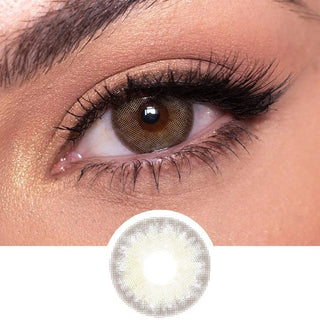 Grey multi-tone contact lens (EyeCandys Isla Mirage Grey) worn on a brown eye with neutral eye makeup and wispy eyelashes, above the eye contact design on a white background.
