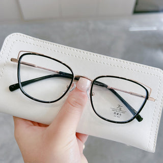 A hand holds EyeCandys Kaylee Cat Eye eyeglasses, featuring black rims with gold accents, resting on a white case; a UV protection label is seen on one lens.