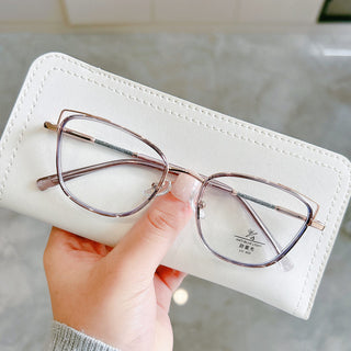 A hand holds a white eyeglasses case with EyeCandys Kaylee Cat Eye transparent-rimmed square glasses on top, set against a light, blurred background.