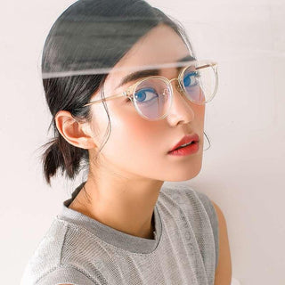 A woman with short dark hair wears EyeCandys Infinity Oversized Oval vintage eyeglasses with clear frames and a light gray top, glancing over her shoulder at the camera as a thin horizontal reflection crosses the image.