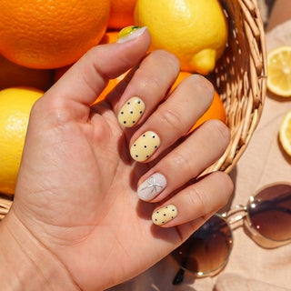 Hand wearing reusable Limoncello press on nails with zesty pastel yellow tone, 3D lemons, bows, polka dots, and gemstone accents for a fun summer look.