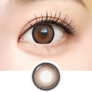 Close-up of an eye wearing i-Sha Dekame Look At Me Sand Brown contacts, showing a subtle limbal ring and long lashes. Below, an enlarged view highlights the gradient design and dekame effect of these i-Sha lenses.