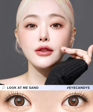 A fair-skinned, blonde woman looks at the camera wearing i-Sha Dekame Look At Me Sand Brown contacts. A close-up reveals her brown eyes and a soft limbal ring. Text: "LOOK AT ME SAND" and "#EYECANDYS". Brand: i-Sha.
