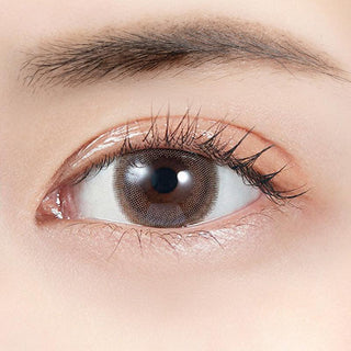 A close-up of a human eye wearing Molak Dark Peony (10pk) by Molak, showing long lashes and a well-groomed brow. The smooth, fair skin highlights the beauty enhanced by these daily color contact lenses.