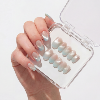 A hand with long, almond-shaped nails in a pearly blue cat-eye gradient holds a clear case of EyeCandys Mist n Fade Press-On Nails, featuring matching handmade press-ons arranged by size.