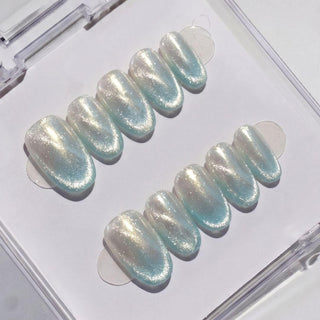 The EyeCandys Moon Glass Press-On Nails set features ten iridescent, pearl-like nails with a subtle blue tint for a salon gel look, all neatly arranged in a clear plastic case against a white background.
