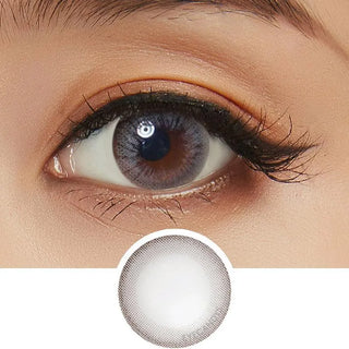 A close-up of an eye wearing NEO Vision Monet Grey (Custom Toric for Astigmatism) lenses by NEO Vision, cosmetic contacts that enlarge the iris with a soft grey hue. Below is a close-up of the lens showing its subtle gray ring design.