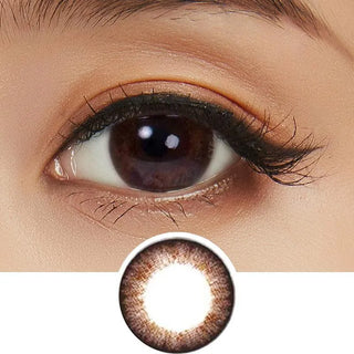 A close-up of a brown eye with long lashes and subtle makeup, wearing NEO Vision Weekly Shiny Dali Brown (12pk) circle lenses by NEO Vision, with the weekly disposables also shown below the eye.