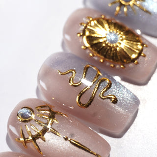 EyeCandys Nyx press on nails featuring translucent taupe lavender cat eye base with sculpted gold celestial sun and star nail art in square shape.