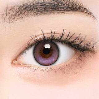 A close-up of a human eye wearing i-Girl One Pick Balance Lavender Mist Purple contacts by i-Girl, surrounded by long lashes and a well-groomed eyebrow, highlights the natural blending effect of these colored lenses.