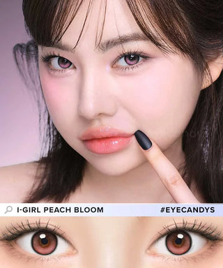 A woman with straight dark hair and peach-toned makeup poses with her finger near her lips. Close-up below shows i-Girl One Pick Balance Peach Bloom Pink lenses, perfect for eye enlargement. Text reads “i-Girl” and “#EYECANDYS.”.