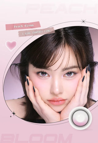 A young woman with straight dark hair rests her face in her hands, wearing i-Girl One Pick Balance Peach Bloom Pink contacts and glossy makeup. The background is pink with graphics and the i-Girl brand name.