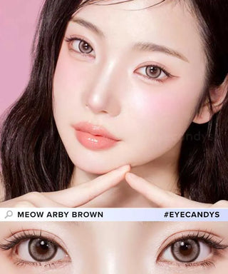 A woman with fair skin and long dark hair poses with a triangle gesture under her chin, wearing natural makeup and Olola Meow Vivid Aby Brown myopia prescription contacts. A close-up of her brown eyes is shown below. Text reads "Olola #EYECANDYS.