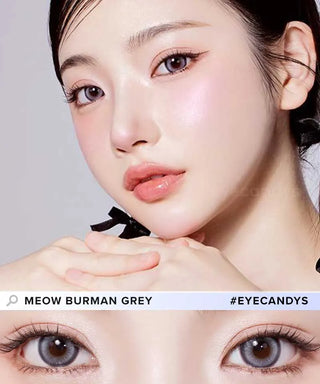 A woman with smooth, fair skin and glossy pink makeup wears Olola Meow Vivid Burman Grey color contacts by Olola. A close-up highlights her light grey eyes. Text: "MEOW BURMAN GREY #EYECANDYS." Perfect for dark eyes.