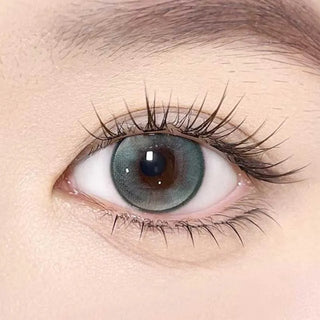 A close-up of a human eye with long lashes wearing Olola Meow Vivid Havana Green color contacts by Olola, showcasing the vibrant iris and detailed skin.