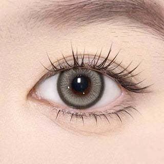 A close-up of a human eye with long lashes wearing Olola Meow Vivid Rubl Green contacts by Olola, highlighting the detailed iris patterns. The smooth, light skin accentuates the vivid color of these prescription colored lenses.