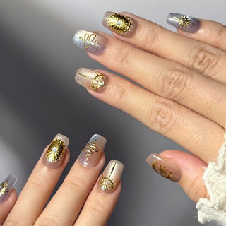 Close up hand showcasing EyeCandys Nyx press on nails featuring sheer cat eye nails with sculpted gold celestial motifs.