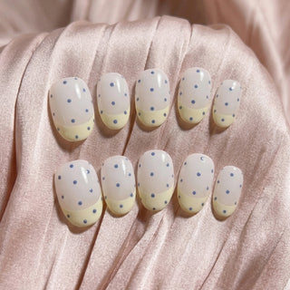 Sunday Dots press on nails by EyeCandys featuring off-white base, pastel yellow French tips, and periwinkle polka dots for a cute, wearable pastel manicure.