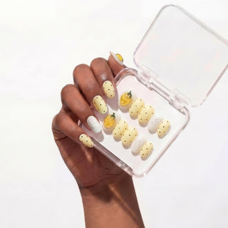 Hand wearing EyeCandys Limoncello press on nails featuring pastel yellow base with 3D lemons, polka dots, bows, and gemstone accents for a playful manicure.