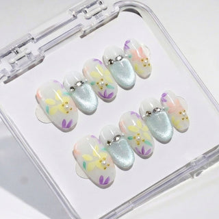 Short oval press on nails Floreline with soft milky base, delicate pastel flowers, and mint shimmer accent nail with pearl and gold bead details.