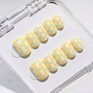 Short round press on nails Sweet Disposition with butter yellow and white vertical stripes and scattered baby blue polka dot design.
