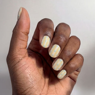 Hand wearing EyeCandys Sweet Disposition press on nails featuring butter yellow and white stripes with baby blue polka dot accents.