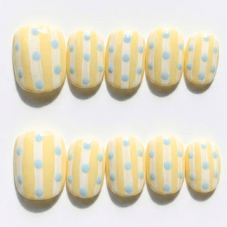 Sweet Disposition press on nails by EyeCandys featuring butter yellow and white striped nails with baby blue polka dots in a retro summer aesthetic.