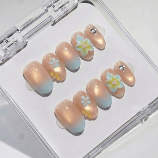 Almond press on nails Lei’d Back with soft nude base, golden shimmer gradient, baby blue tips, and sculpted 3D plumeria flower nail art.