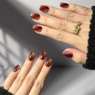 Hand wearing EyeCandys Night Plum press on nails featuring marbled plum tones with warm auburn depth.