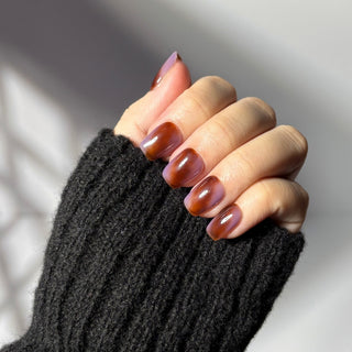 Hand showcasing EyeCandys Night Plum marbled press on nails in deep plum and auburn shades.